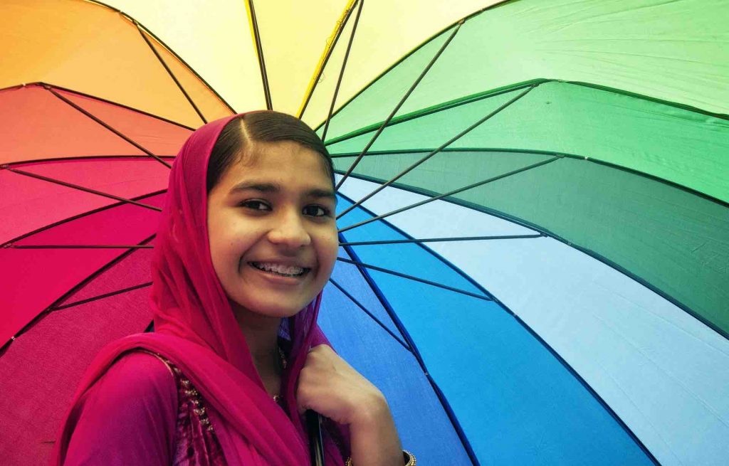 Woman with braces smiling in front of a colorful umbrella